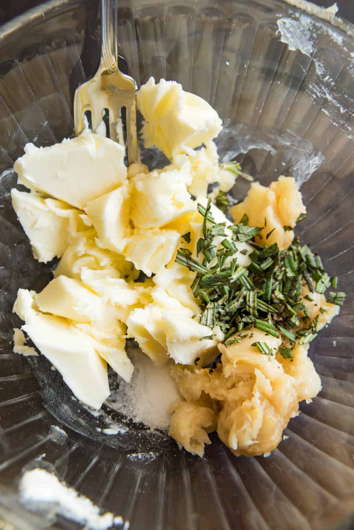 Ingredients for a roasted garlic & rosemary compound butter in a bowl together ready to be mashed.