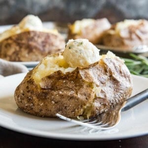 Baked potatoes on plates with scooped balls of butter on top.