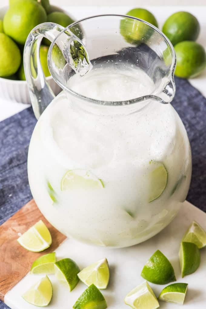 a glass pitcher filled with brazilian limeade and sliced limes