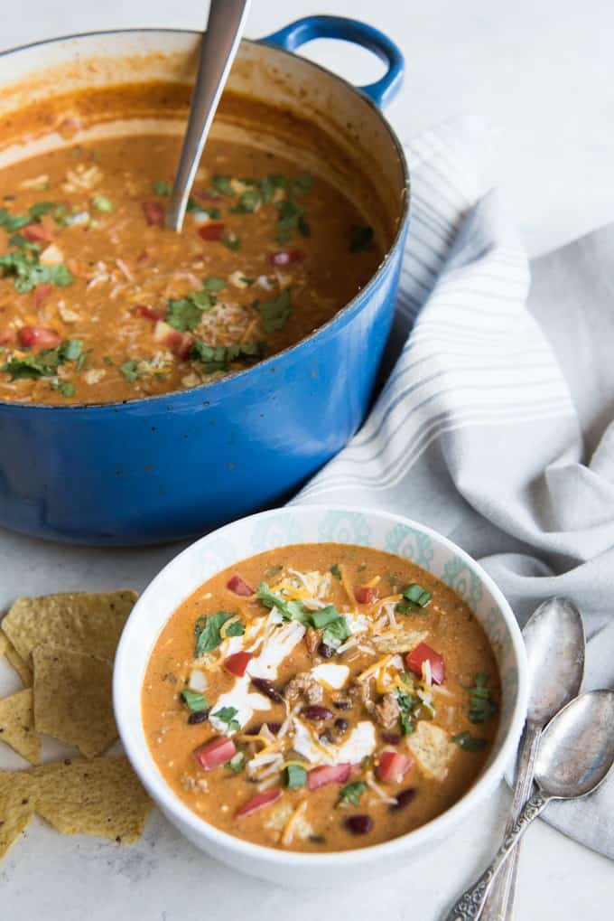 large blue pot of taco soup next to a bowl of garnished taco soup and spoons