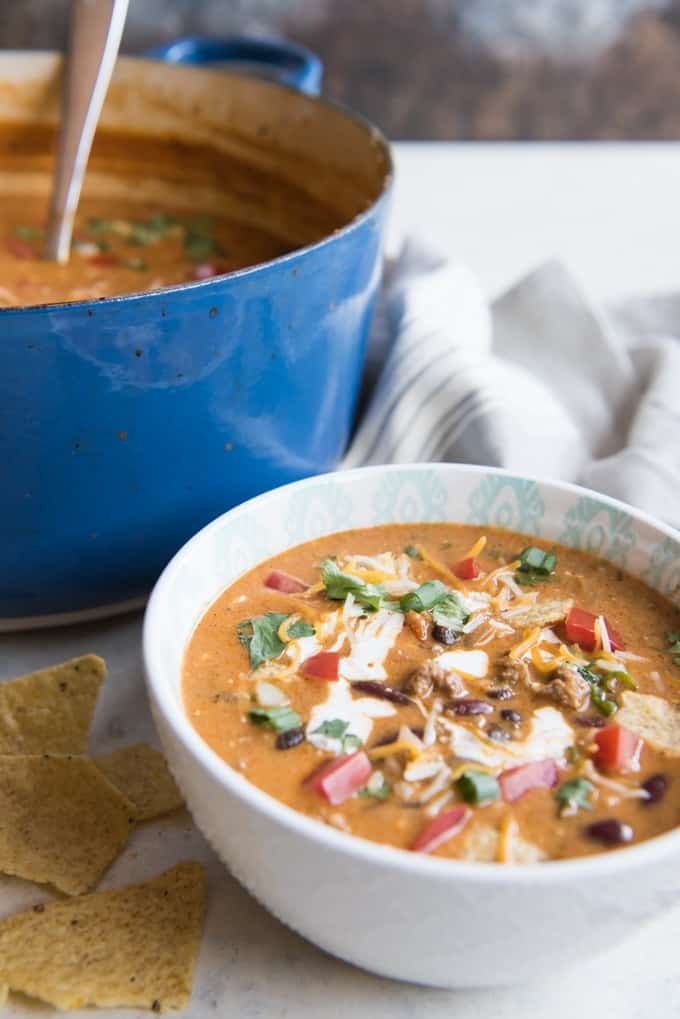 white bowl of taco soup next to a large blue pot of soup