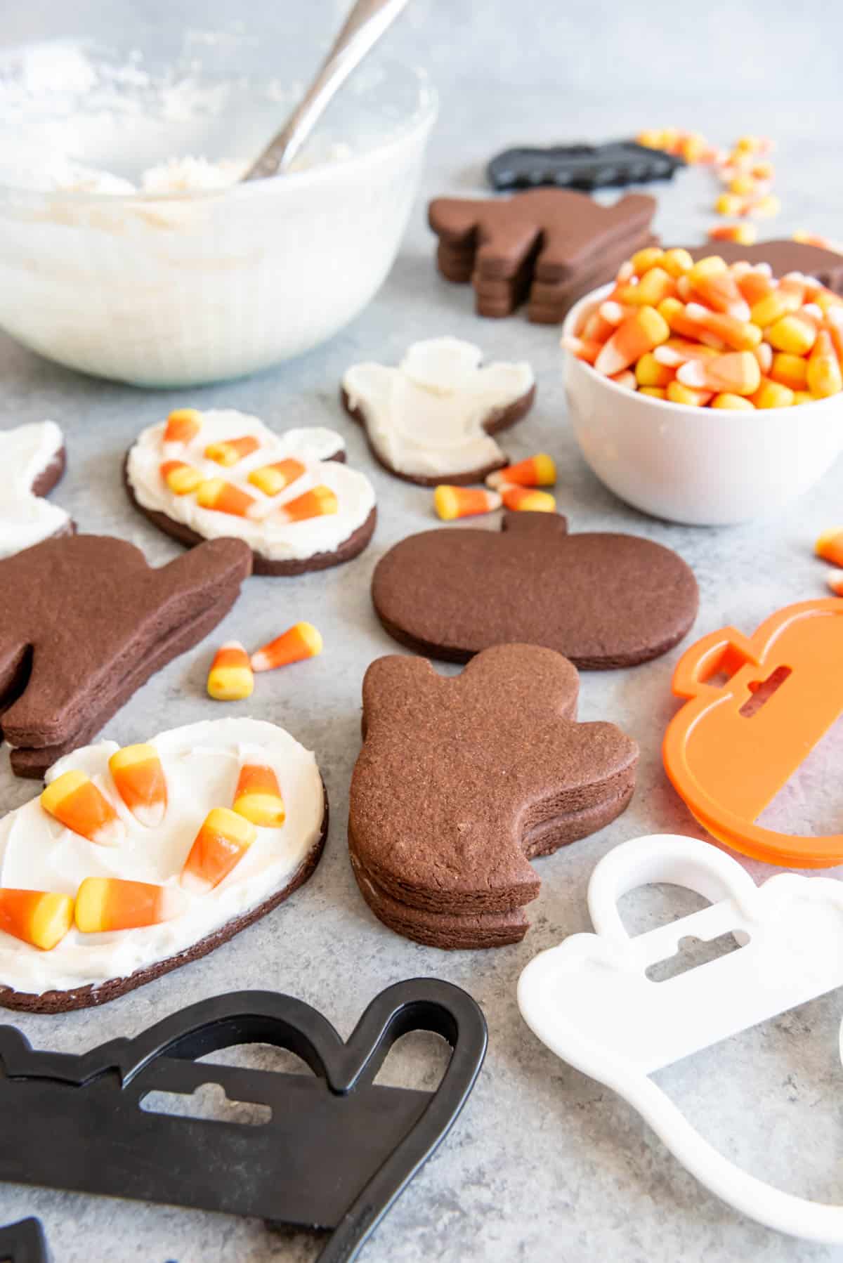Bowls of candy corn and frosting used to decorate Halloween chocolate cut out sugar cookies.