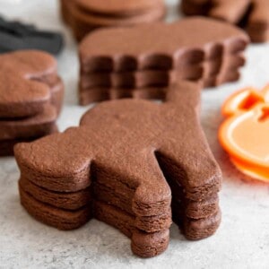 Stacks of chocolate cut out sugar cookies in Halloween shapes.