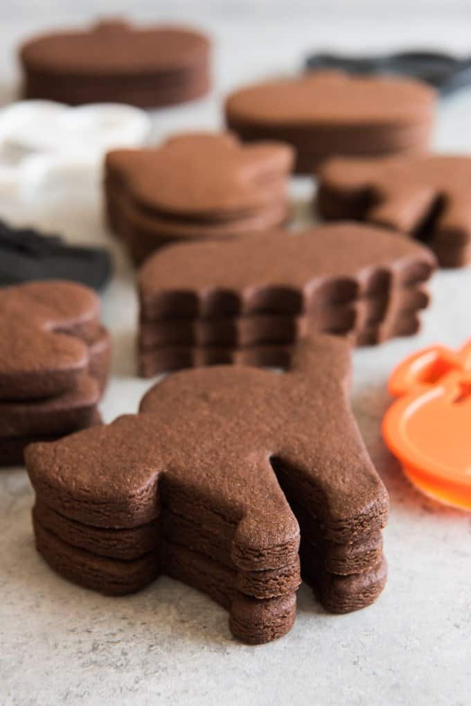 Stacks of unfrosted chocolate cut out sugar cookies in Halloween shapes.