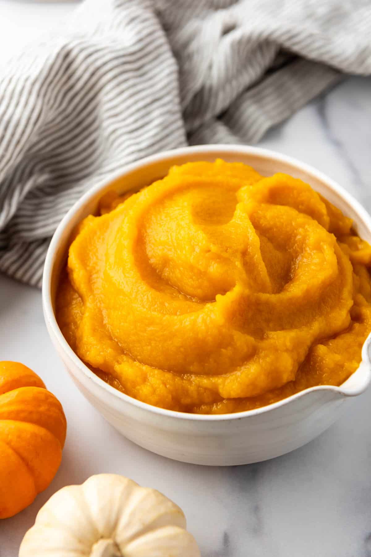 A bowl of homemade pumpkin puree in front of a striped linen napkin.