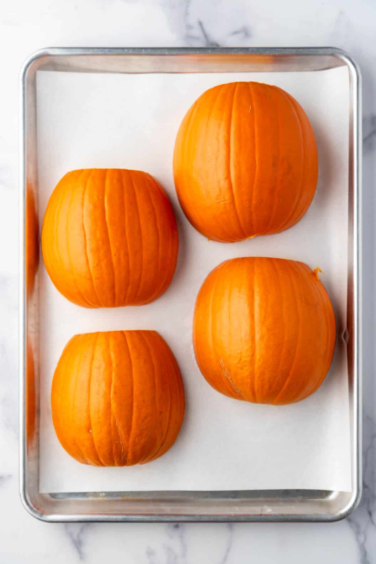 Sugar pumpkin halves on a baking sheet lined with parchment paper.