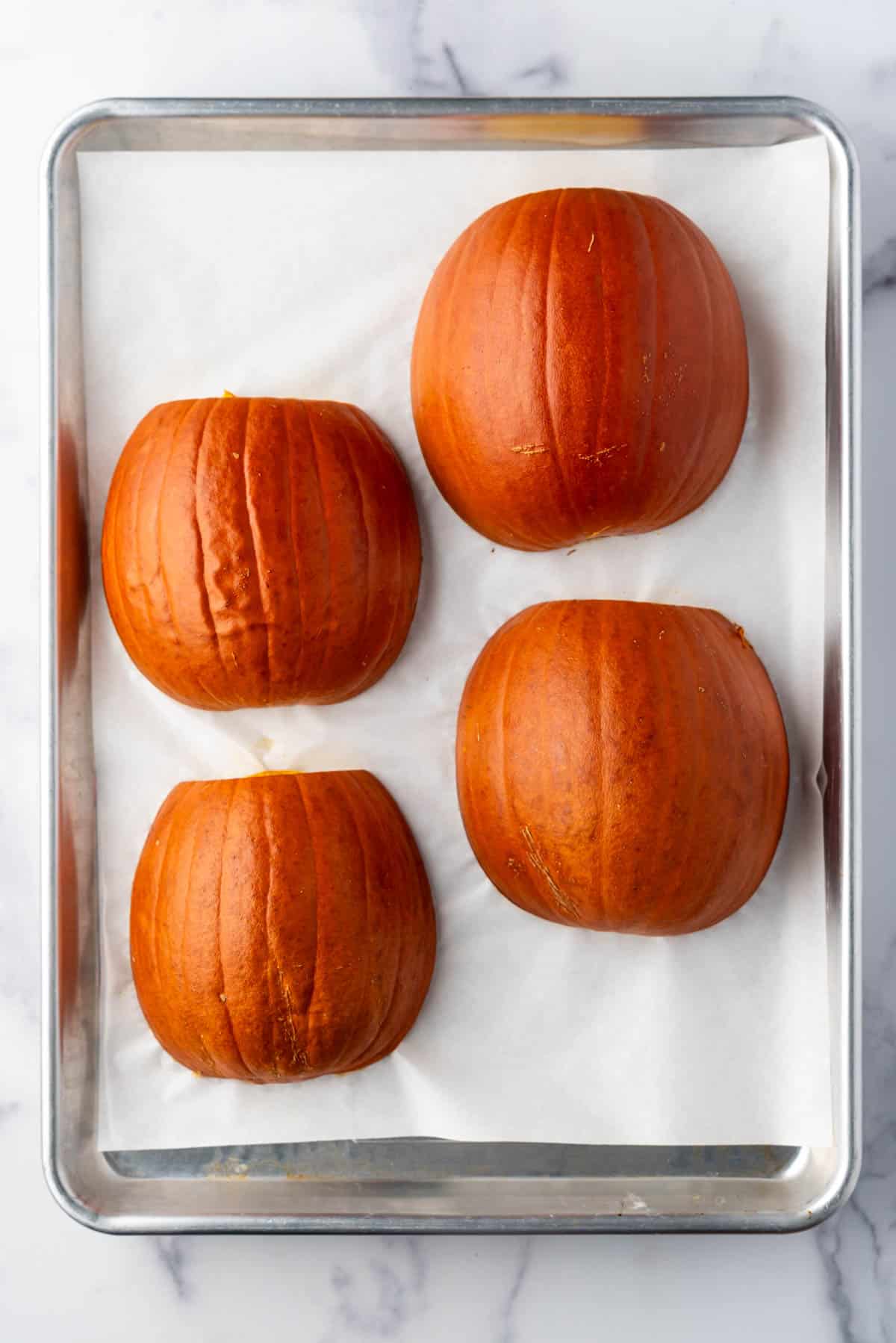 Roasted sugar pumpkin halves on a baking sheet lined with parchment paper.