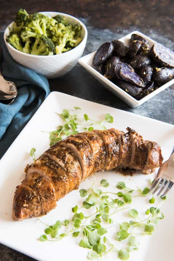 Honey Mustard Pork Tenderloin served family style with Honey Steamed Broccoli and Roasted Baby Purple Potatoes in serving dishes behind it.