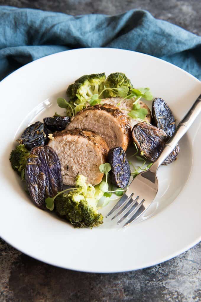 Beautifully plated and presented dish of sliced honey mustard pork tenderloin with a few garlic, rosemary and thyme roasted baby purple potatoes and broccoli.