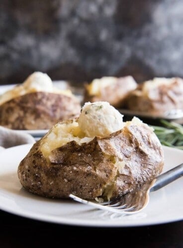 baked potatoes on plates with scooped balls of butter on top