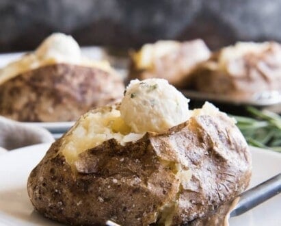 baked potatoes on plates with scooped balls of butter on top