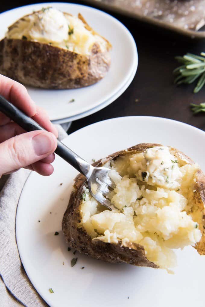 Hand holding a fork digging into a fluffy salt crusted baked potato side dish.