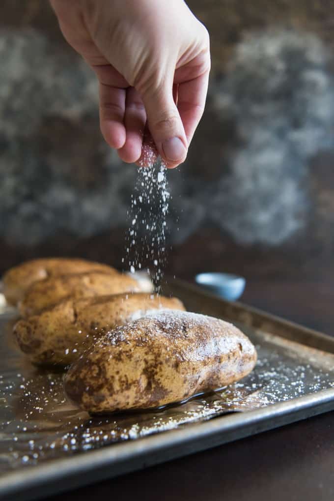 Hand drizzling coarse salt over an oil rubbed russet potato.