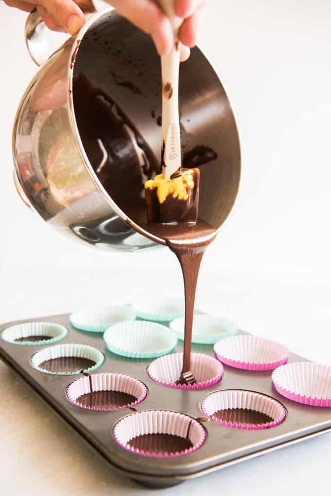 Ribbon of chocolate cake batter being poured from the bowl into cupcake liners halfway full before baking.