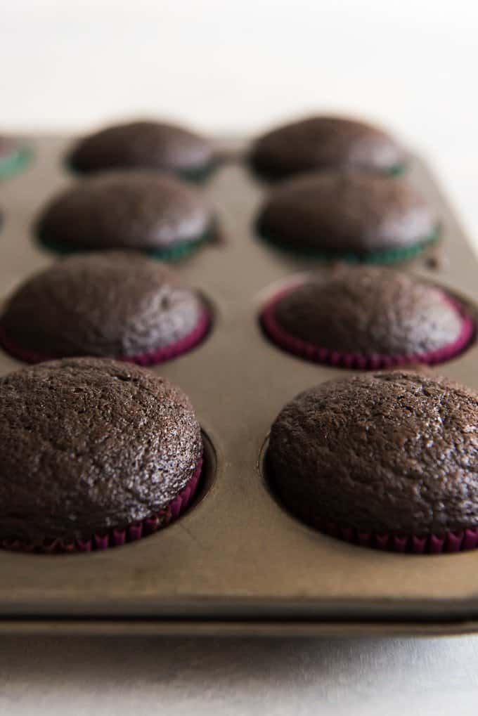 Domed moist chocolate cupcakes in a cupcake pan before being frosted.