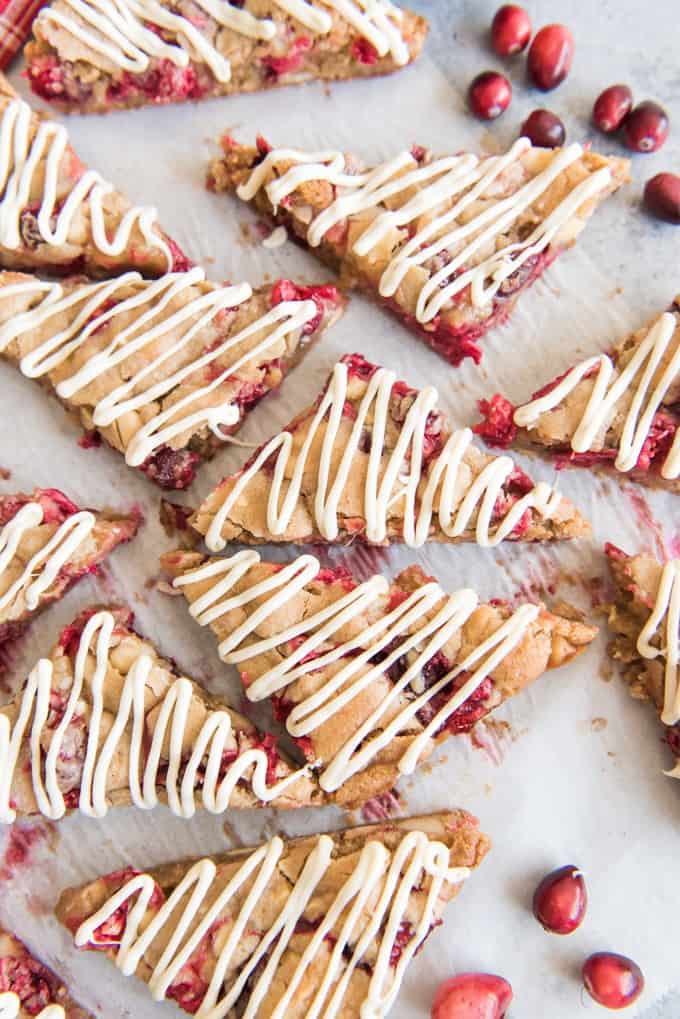White Chocolate Cranberry Blondies are cut into triangle shaped bars and then drizzled with melted white chocolate and displayed on parchment paper.
