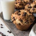 Chocolate chip muffins on a wooden board with a glass of milk and scattered chocolate chips around it