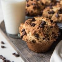 Chocolate chip muffins on a wooden board with a glass of milk and scattered chocolate chips around it