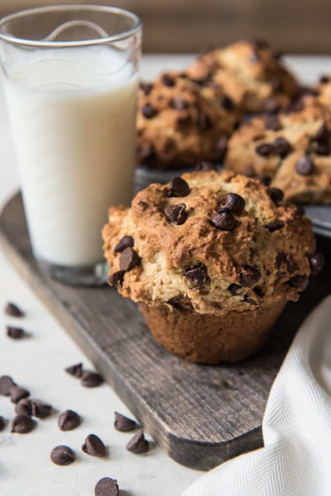 Chocolate chip muffins on a wooden board with a glass of milk and scattered chocolate chips to the side