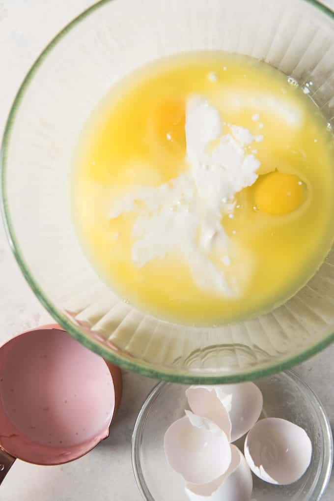 a glass bowl with eggs and other ingredients inside, a measuring cup and egg shells off to the side