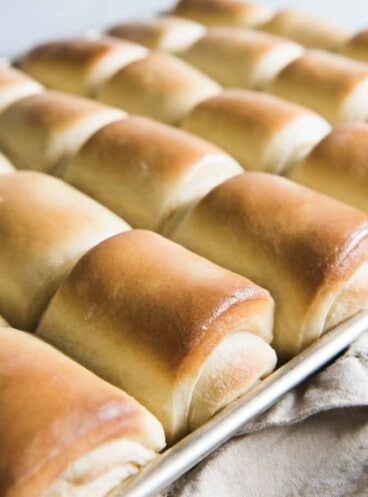 a baking sheet with rows of baked lion house dinner rolls on it