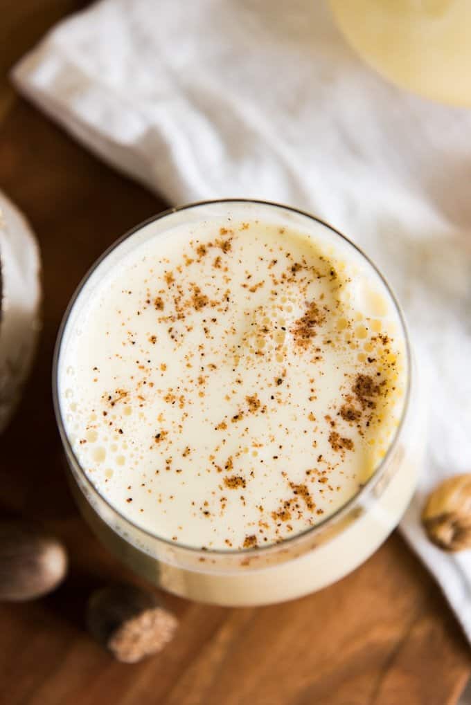 An aerial view of the nutmeg on top of the eggnog in a glass with a white towel off to the side