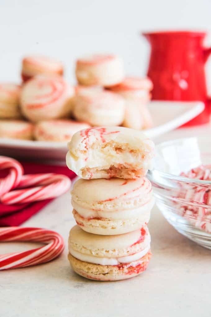 stacked peppermint macarons next to peppermint candies and a plate of more macarons in back with a red pitcher