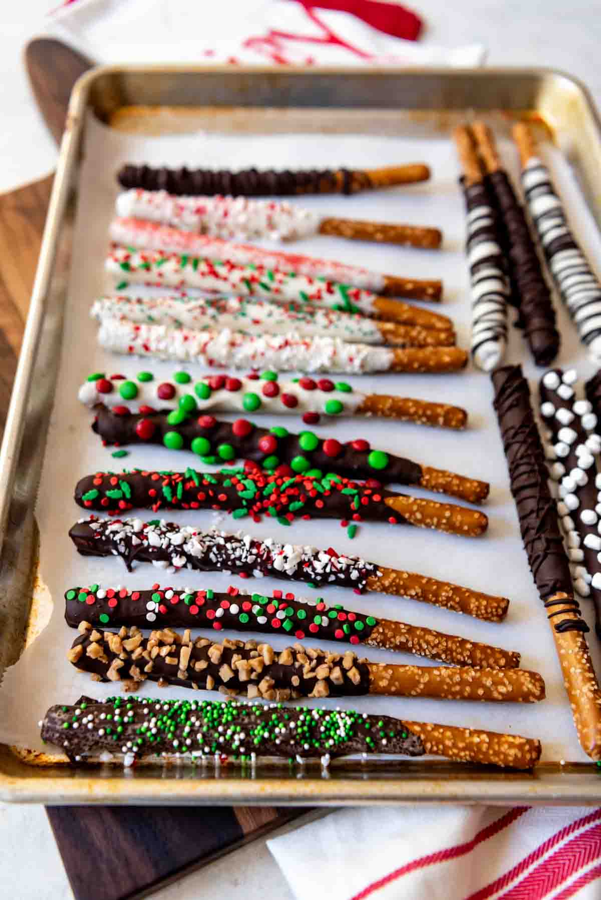 A parchment lined baking sheet with chocolate coated pretzel rods covered in sprinkles and other goodies.