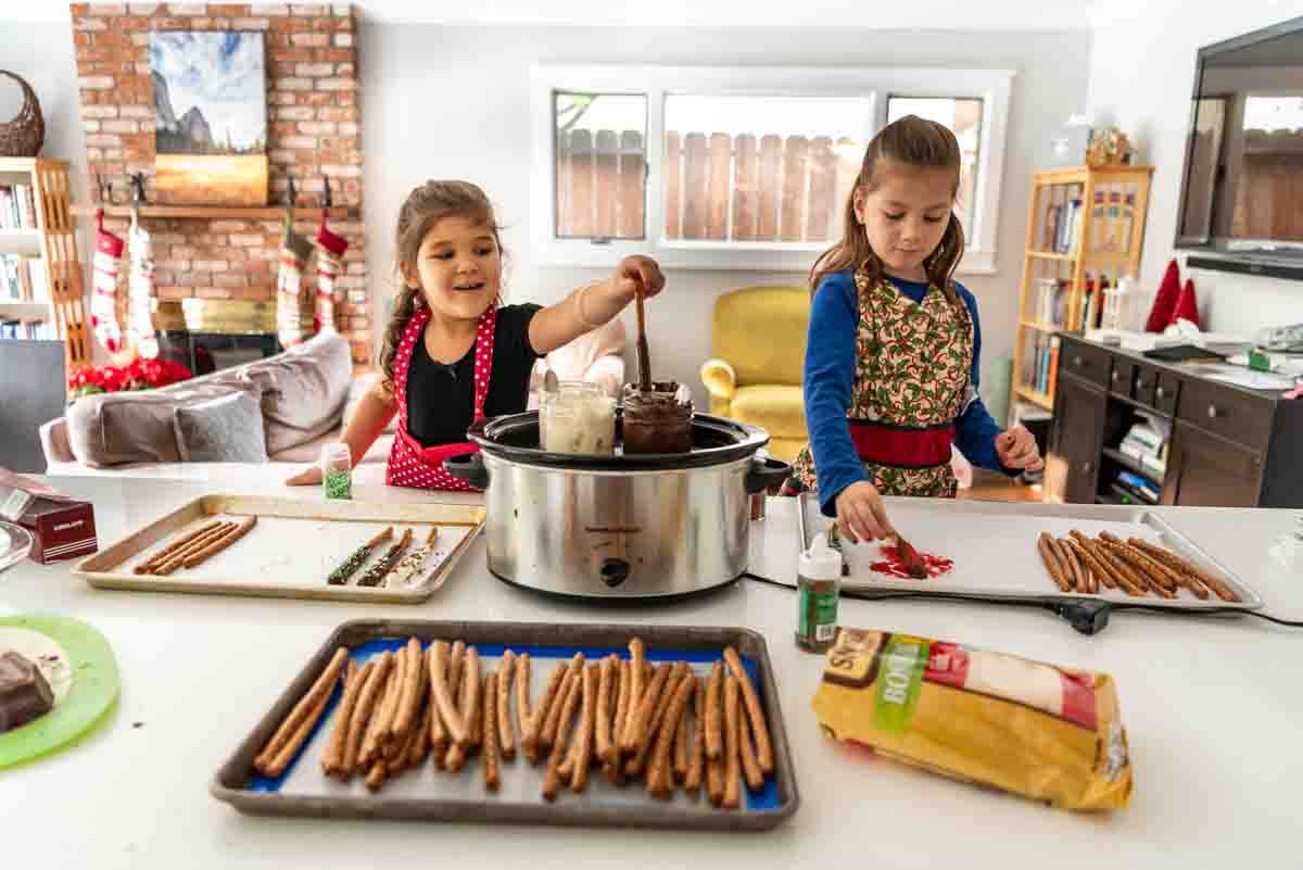 Dipping pretzel rods in chocolate melted in a slow cooker for a fun Christmas treat that's perfect for the kids to make!