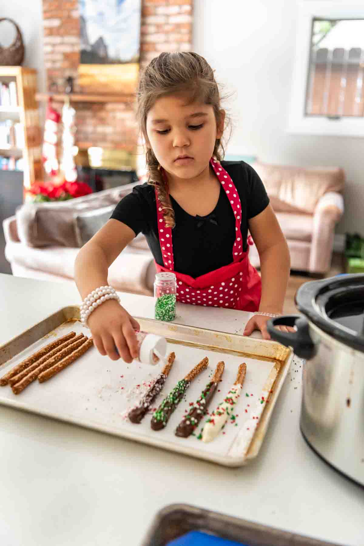 Adding sprinkles to chocolate covered pretzel rods.