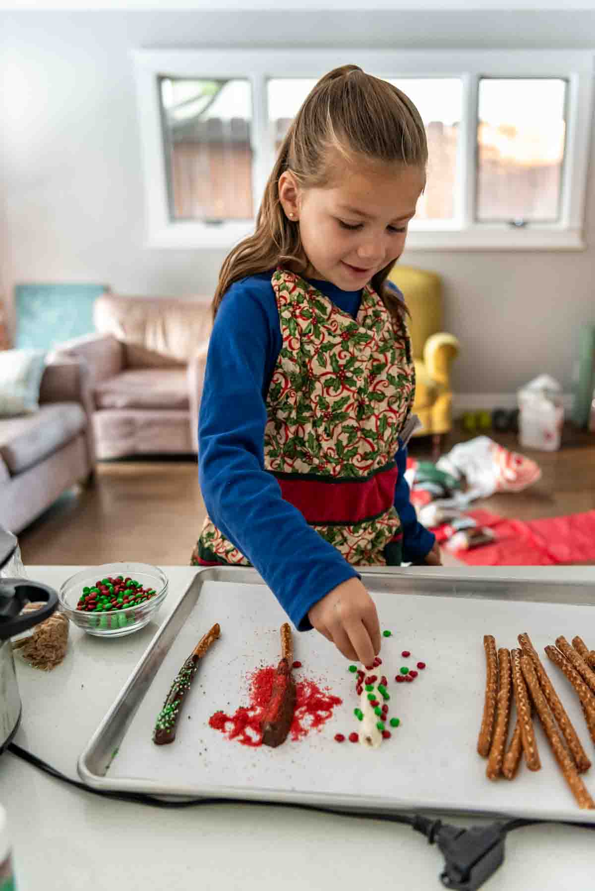 Sprinkling mini M&M's over a white chocolate covered pretzel rod.