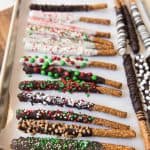 a parchment lined baking sheet with chocolate coated pretzelrods covered in sprinkles and other goodies