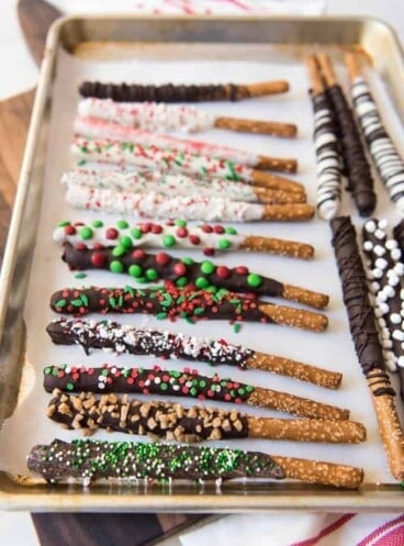 a parchment lined baking sheet with chocolate coated pretzelrods covered in sprinkles and other goodies