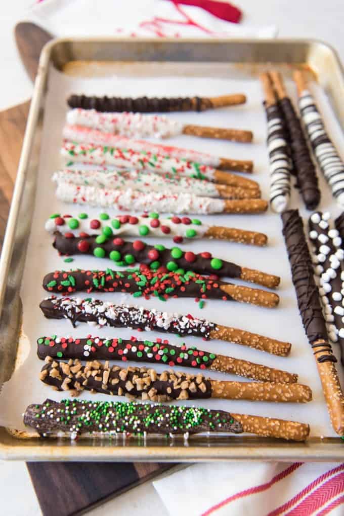 a parchment lined baking sheet with chocolate coated pretzel rods covered in sprinkles and other goodies