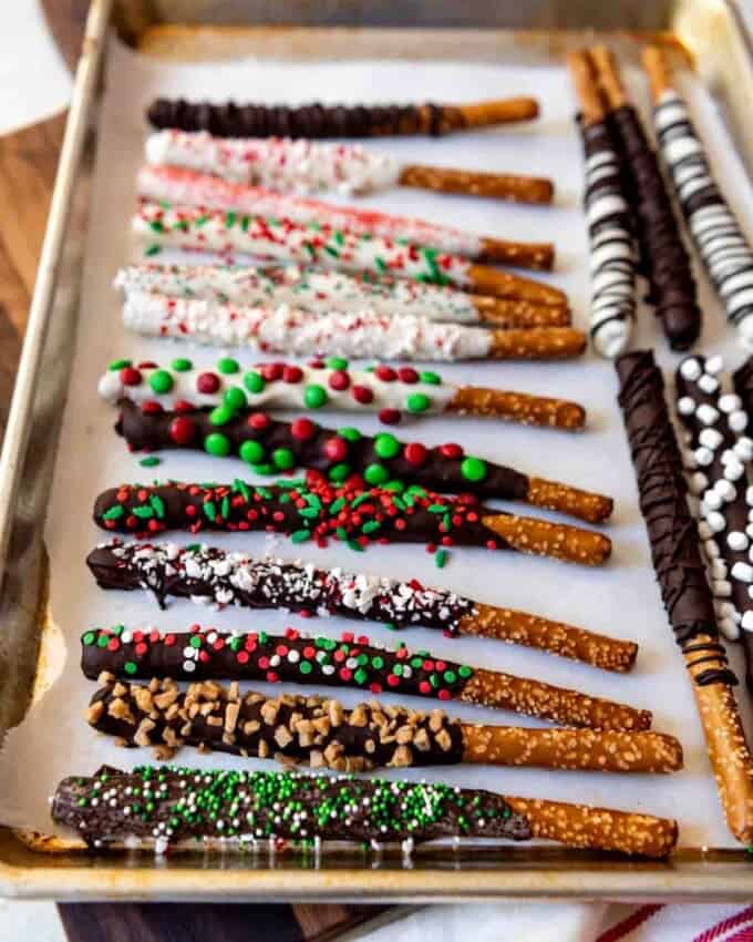 A parchment lined baking sheet with chocolate coated pretzel rods covered in sprinkles and other goodies.