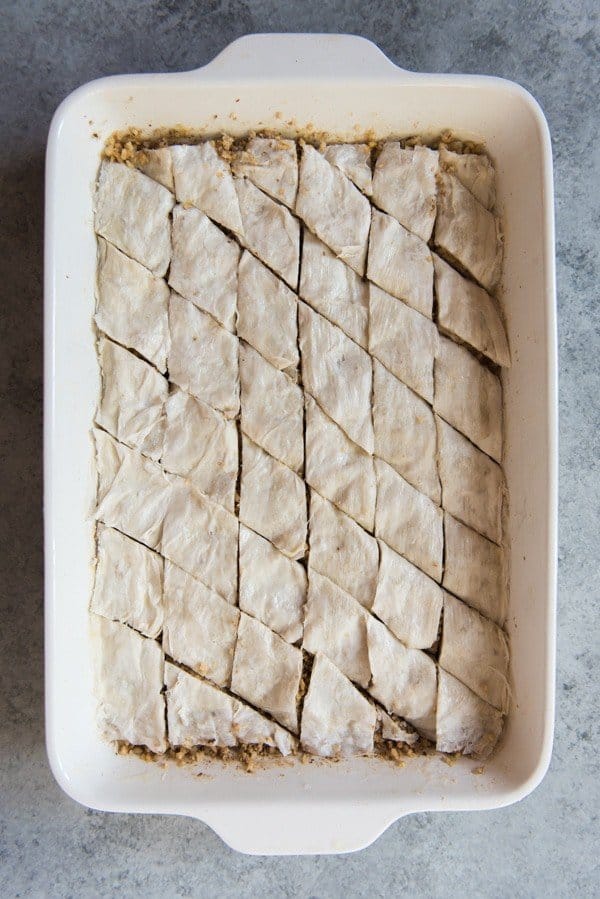 Unbaked baklava in a white baking dish cut into diamond