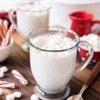 twoglass mugs filled with white hot chocolate and scattered marshmallows and peppermint to the sides