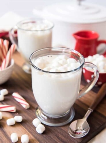 twoglass mugs filled with white hot chocolate and scattered marshmallows and peppermint to the sides