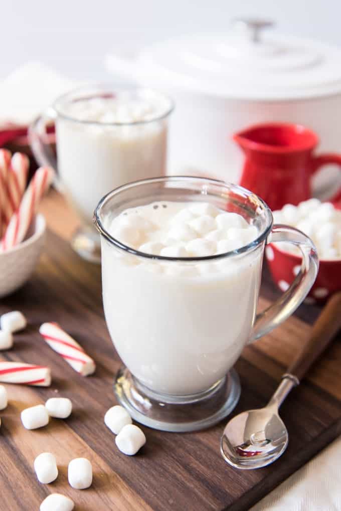 two glass mugs filled with white hot chocolate and scattered marshmallows and peppermint to the sides
