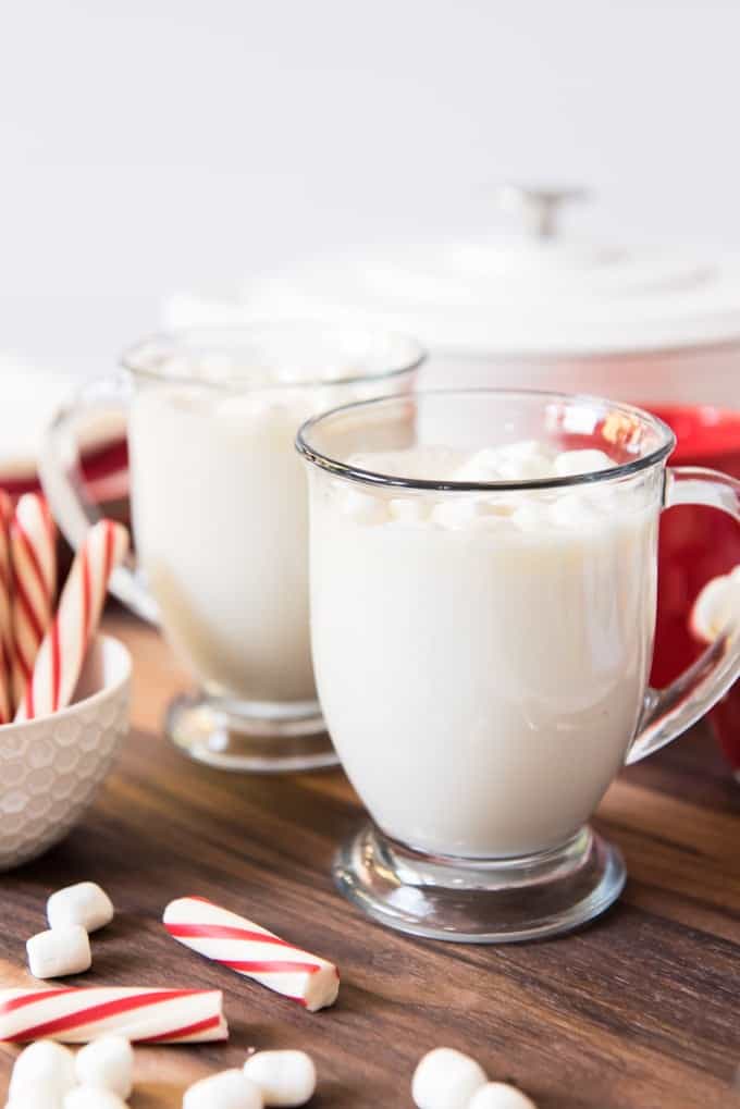 two glasses of hot white chocolate drink next to marshmallows and candy canes