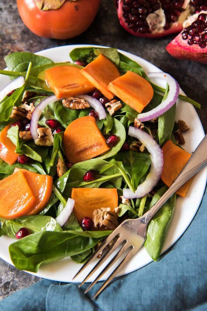 a white plate with Pomegranate, Spinach, & Persimmon Salad and a fork