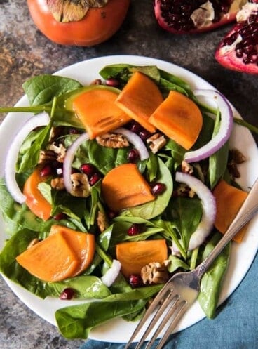 a festive persimmon and spinach salad with pomegrante seeds