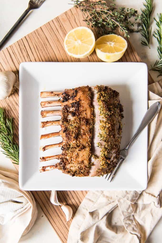 cooked rosemary garlic rack of lamb on white plate with fork