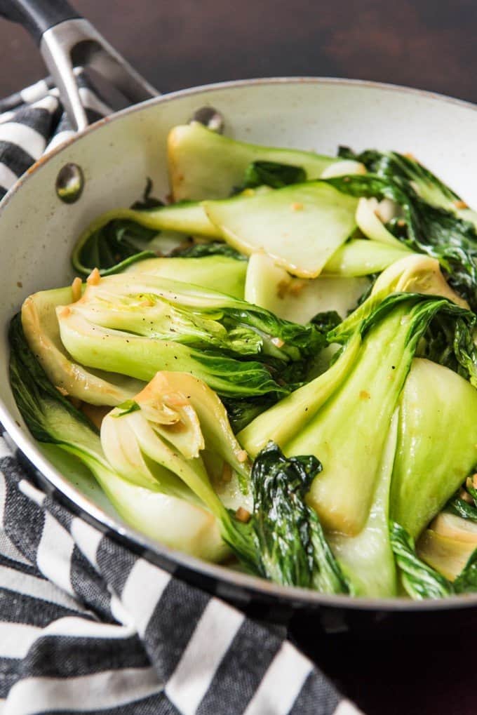 baby bok choy in a skillet on a striped towel