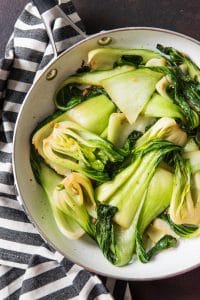 an aerial view of stir fried baby bok choy in a skillet on a striped towel