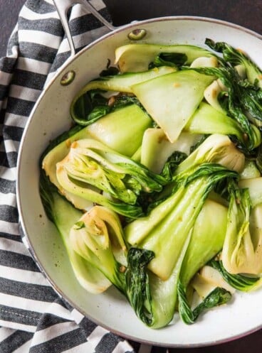 an aerial view of stir fried baby bok choy in a skillet on a striped towel