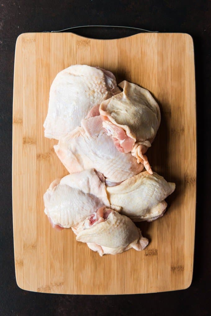 Raw bone-in, skin-on chicken thighs on a wooden cutting board.