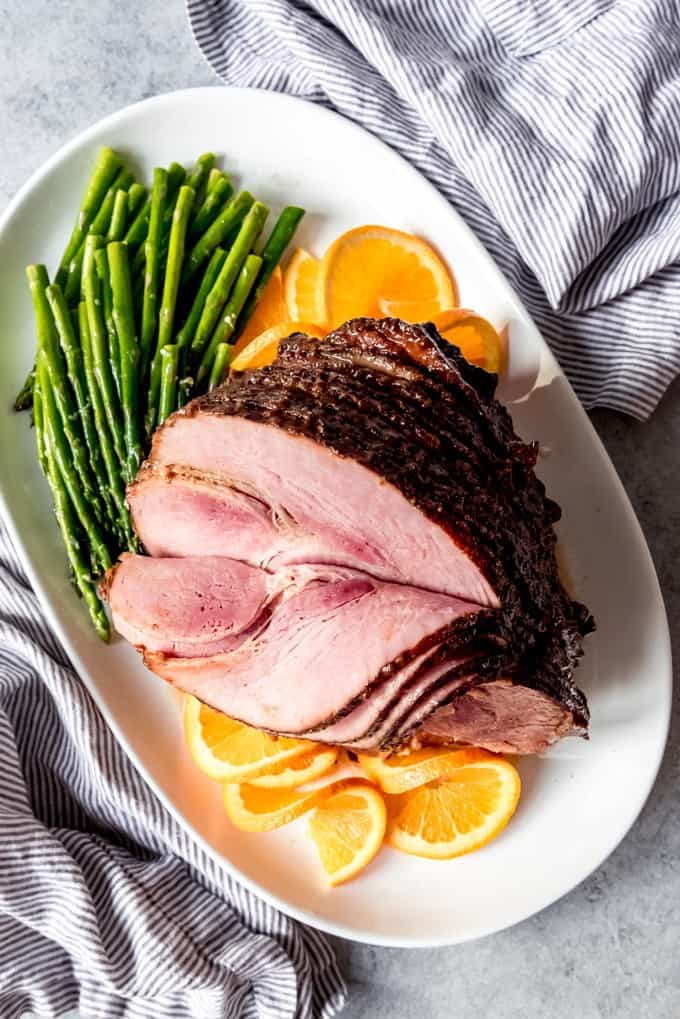 An image of an Easter Ham with Brown Sugar Glaze on a white platter with asparagus and orange slices.