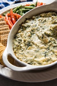 Spinach and Artichoke Dip in a baking dish with crackers and cut vegetables to the side