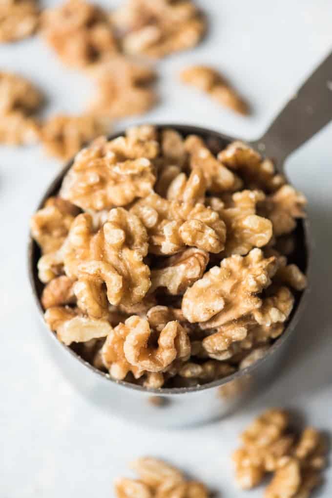 a measuring cup of walnuts with more scattered around